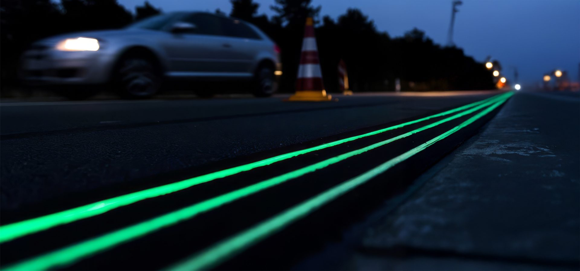 Dark road with three glowing green lines, blurry car and cones.