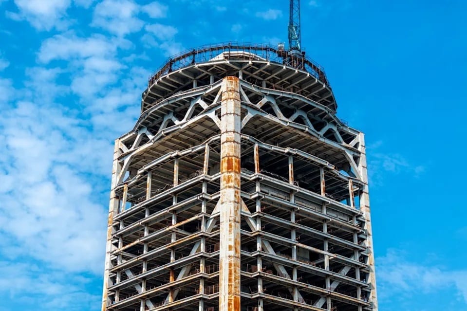 Unfinished skyscraper's intricate frame with a crane, under a blue sky.