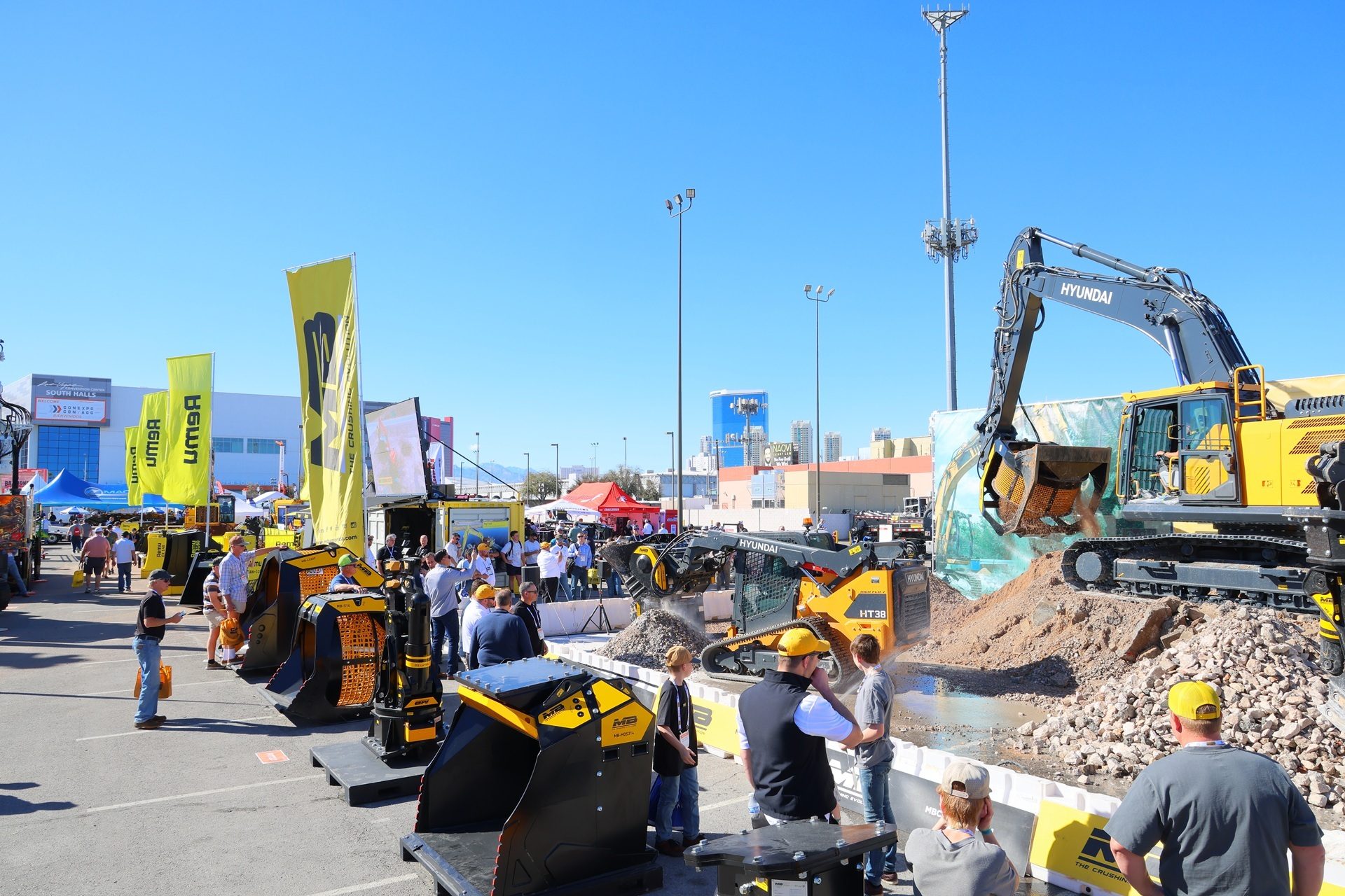 An outdoor construction equipment exhibition with a large excavator, skid steer, and people.