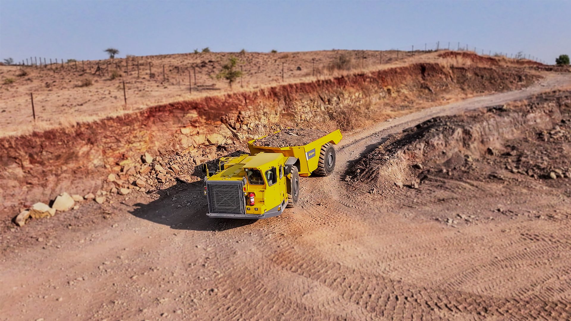 A yellow mining dump truck on a dusty road in an open-pit mine.