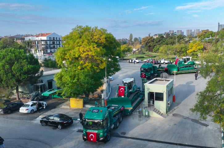 Green trucks transporting bulldozers decorated with Turkish flags in a parking lot.