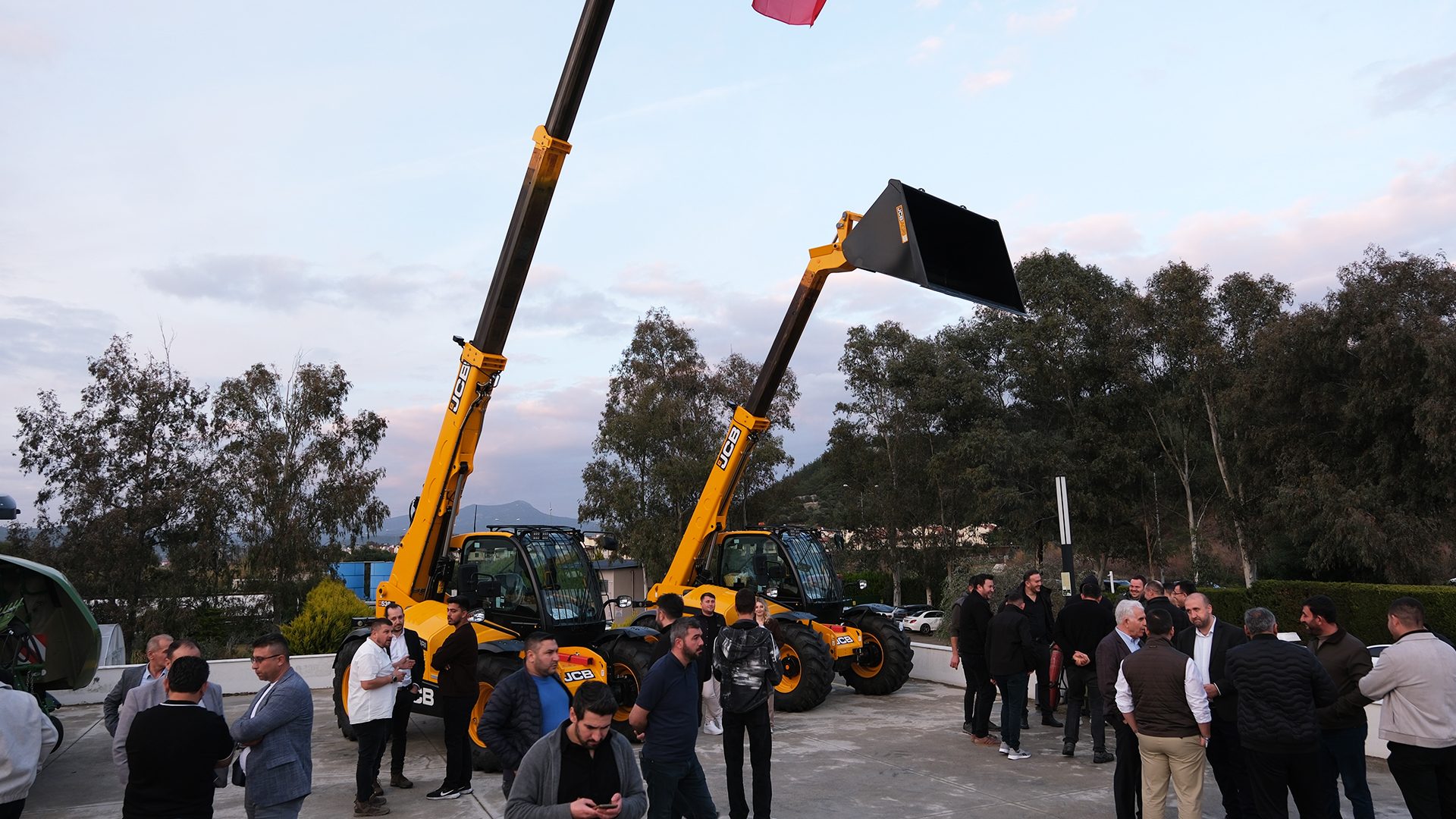 Men gathered outdoors with two yellow JCB telehandlers.