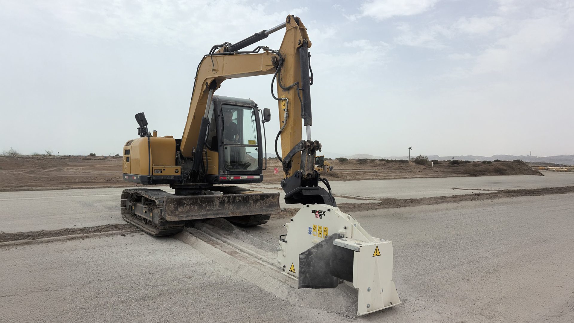 Excavator with a road milling attachment cutting a trench in a paved surface.