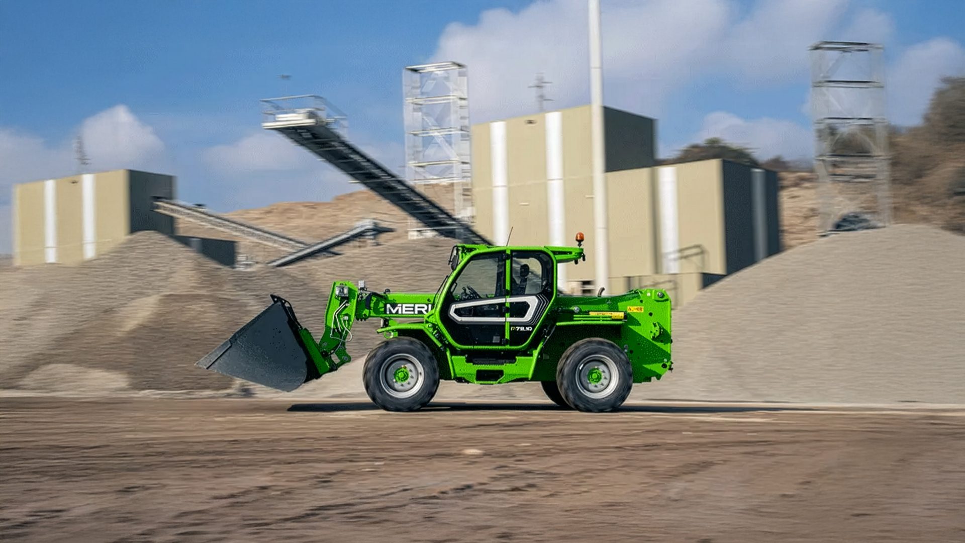 A green telehandler moves across a gravel plant with industrial buildings and conveyor belts in the background.
