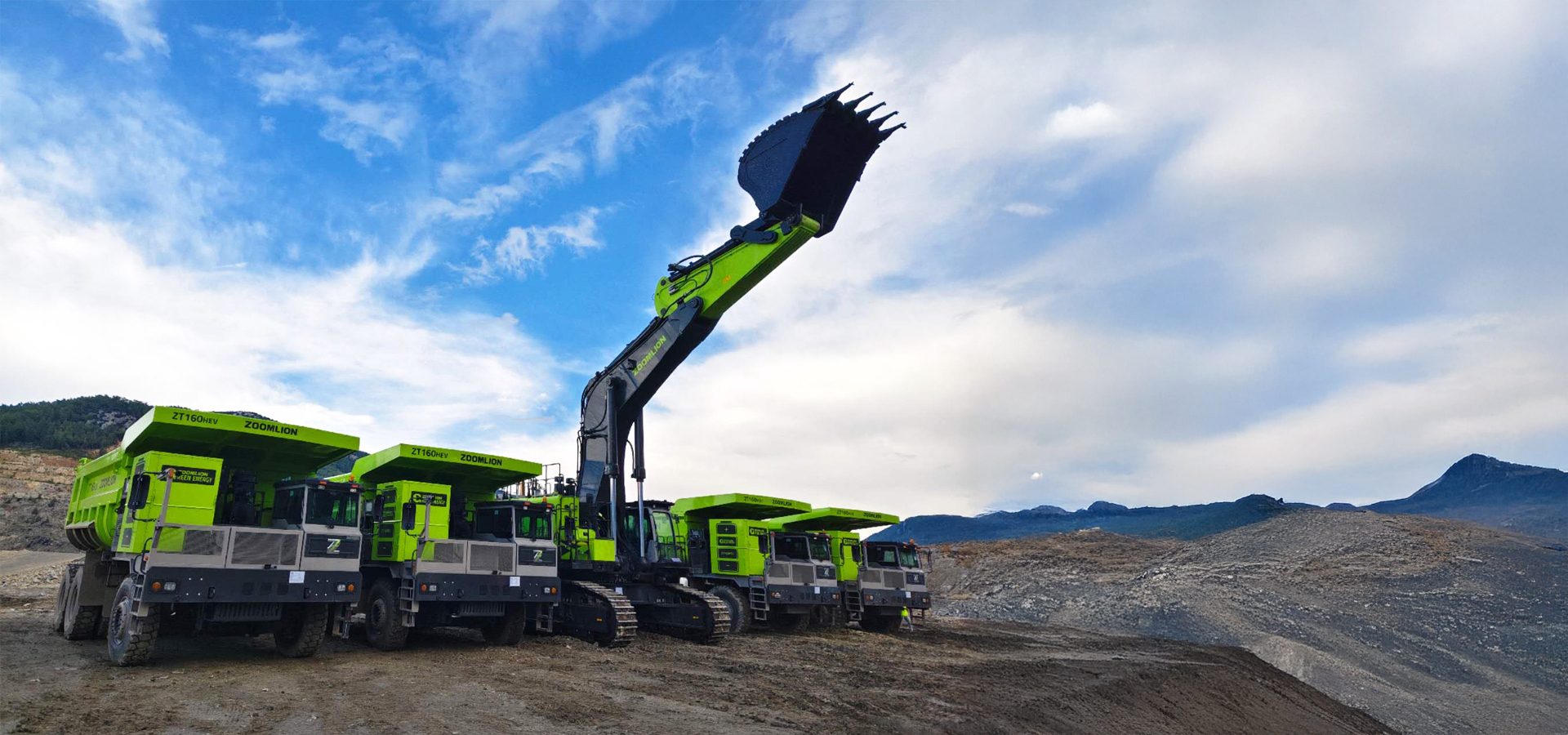 Green Zoomlion heavy machinery, including dump trucks and an excavator, at a rugged site under a cloudy sky.