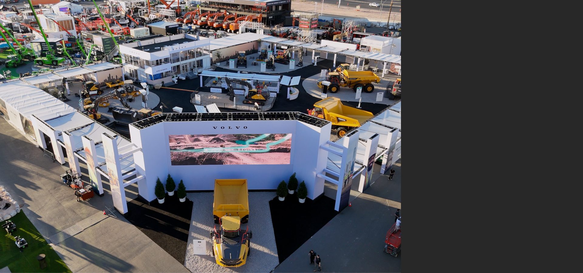 Aerial view of a large Volvo construction equipment exhibit with a giant screen and multiple yellow trucks.
