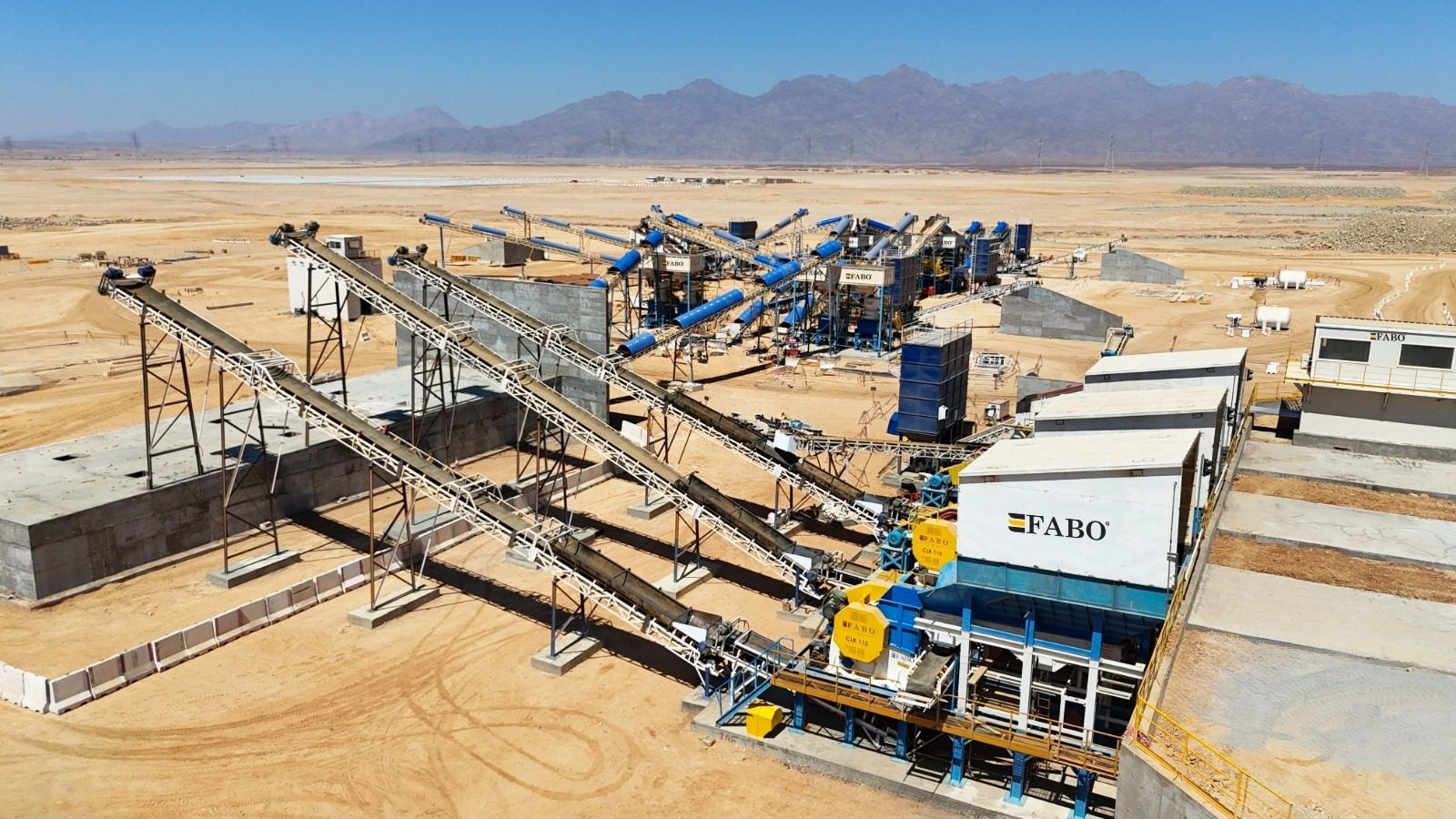 Aerial view of a large mining or quarrying operation with conveyor belts and processing equipment in a desert.