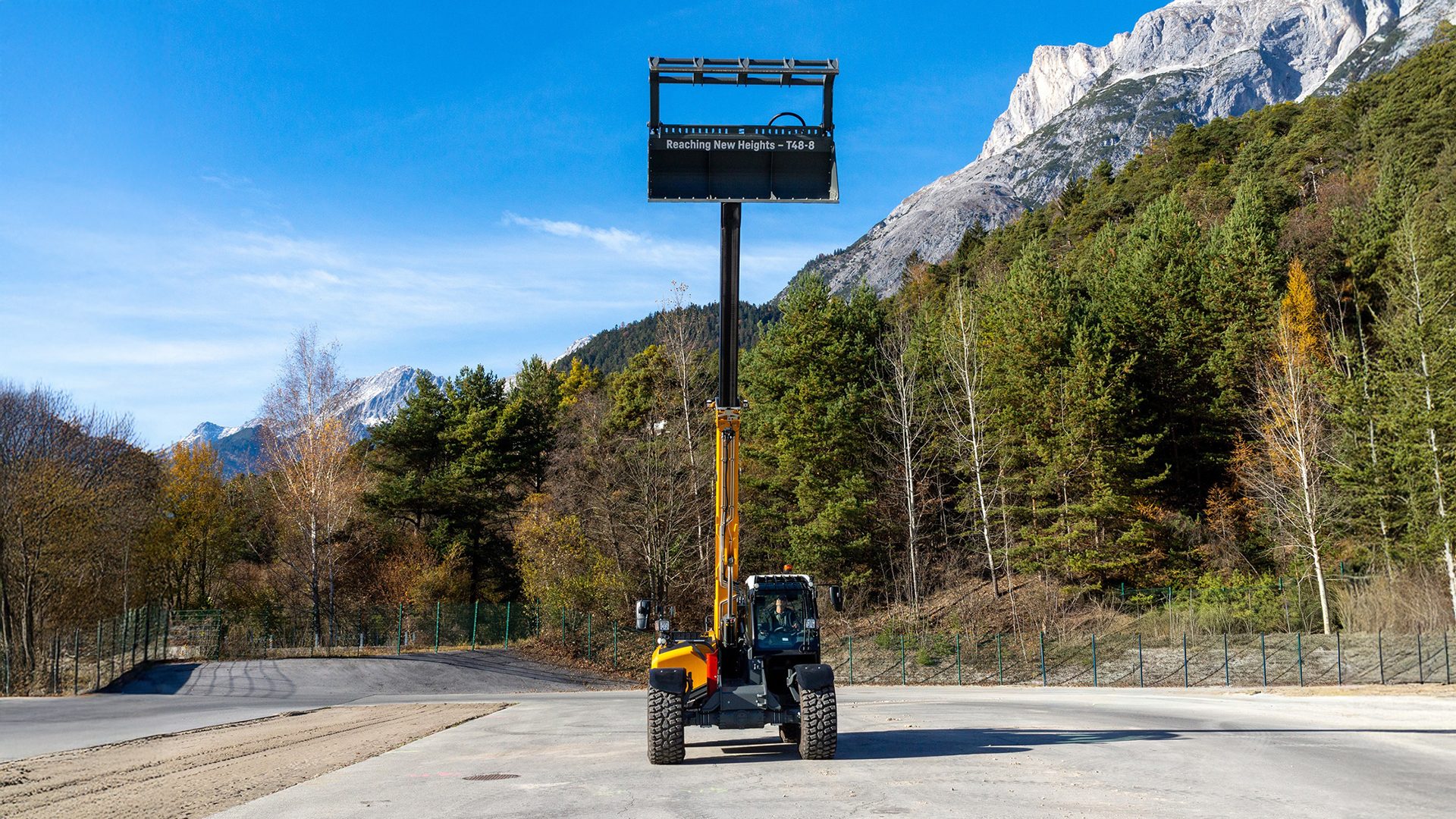 A yellow telehandler with an extended boom displays "Reaching New Heights - T48-8" against mountains.