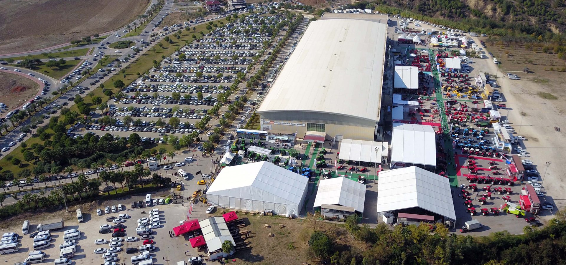 Aerial view of a large exhibition center with outdoor displays of agricultural machinery and crowded parking lots.