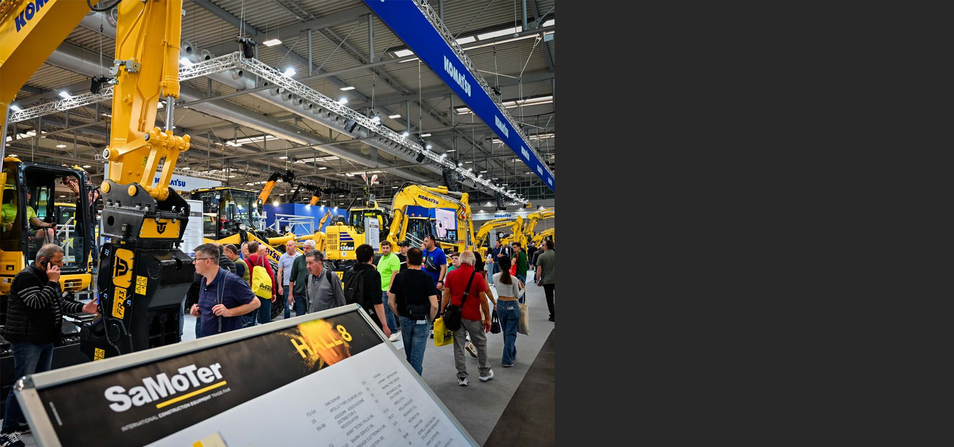 People walk among yellow Komatsu excavators at the SaMoTer international construction equipment trade fair.