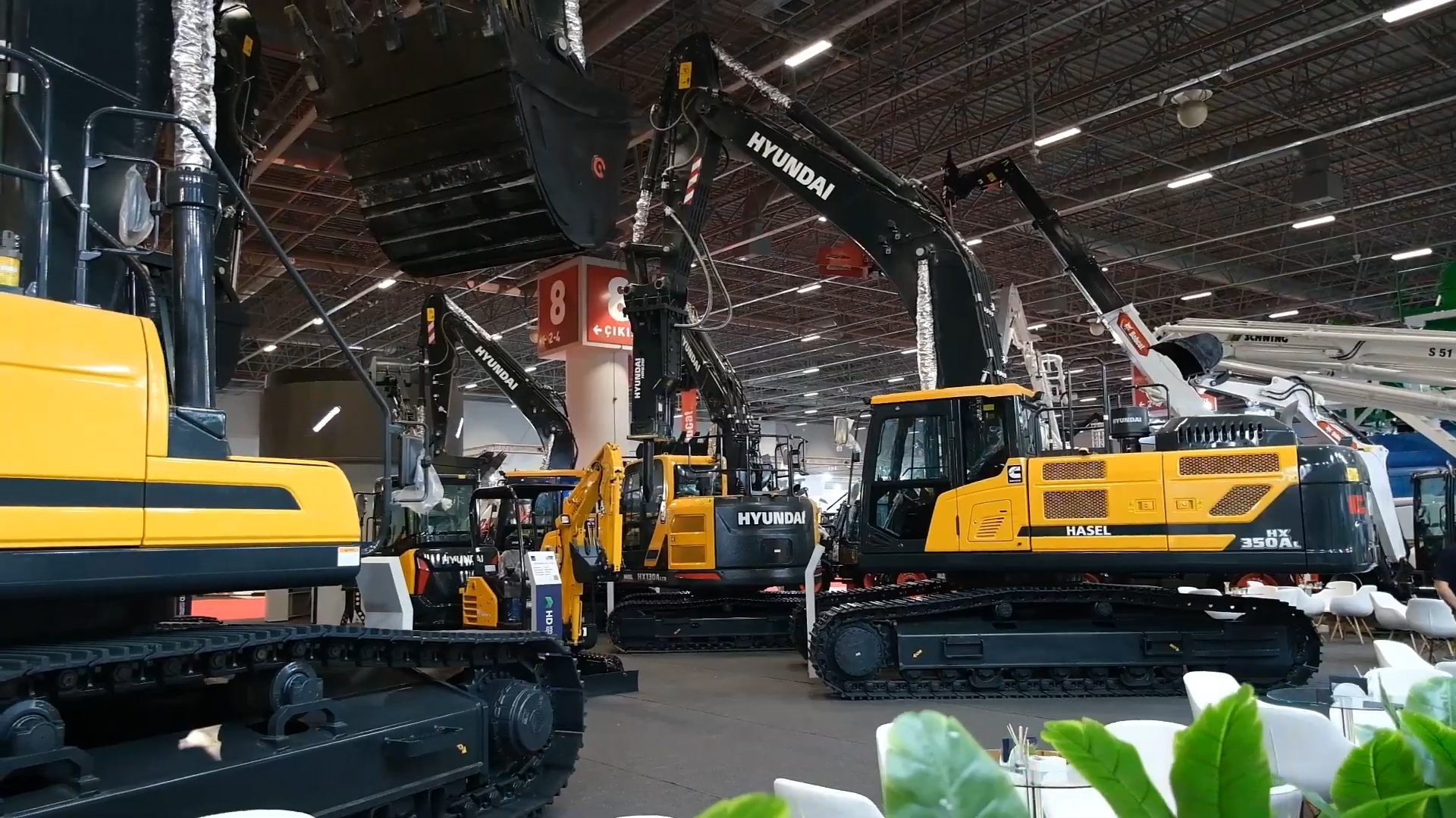 A wide shot of multiple Hyundai excavators and heavy construction machinery displayed at an indoor exhibition.