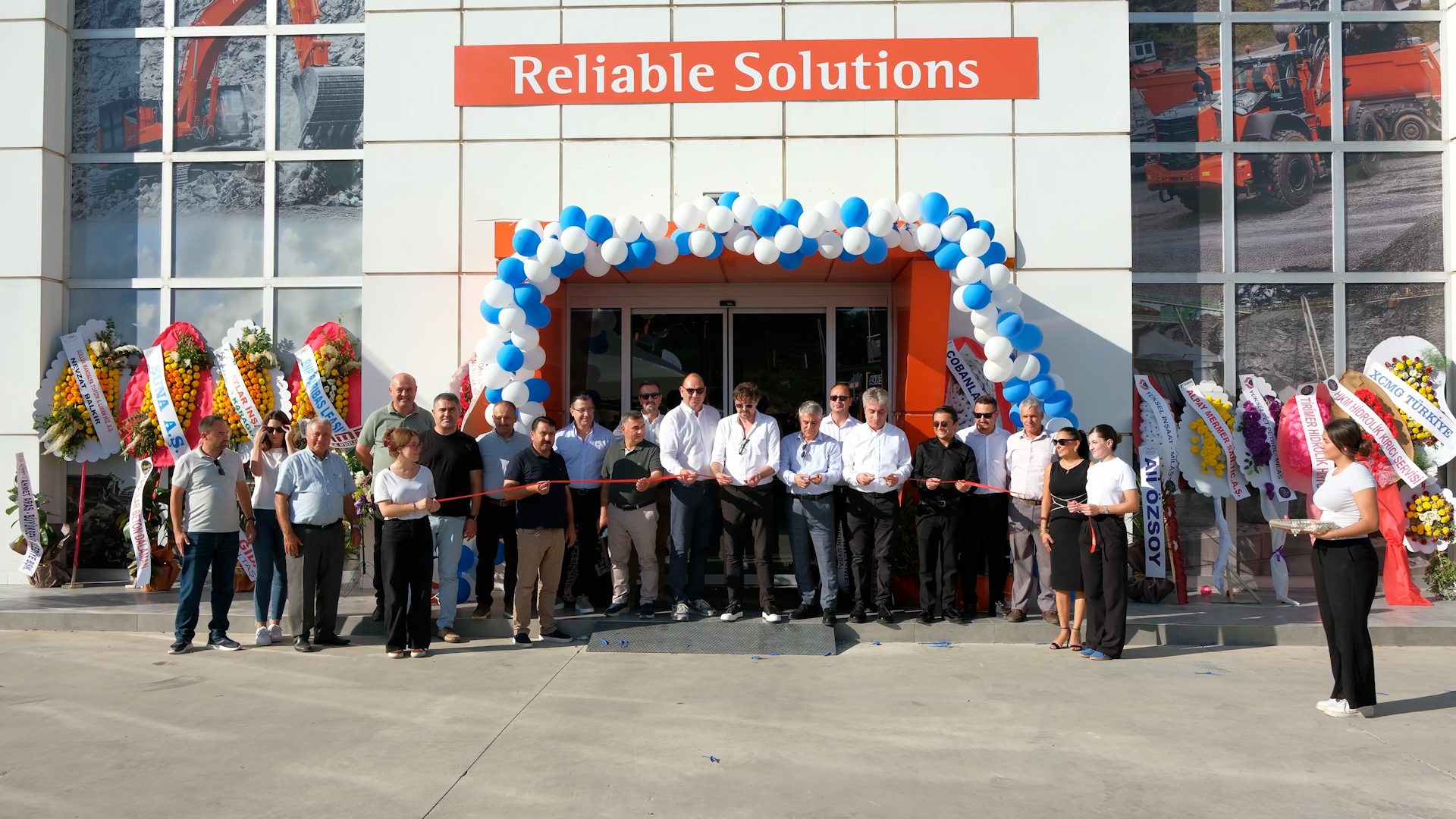 Grand opening ceremony for "Reliable Solutions" with ribbon cutting, people, balloons, and flowers.