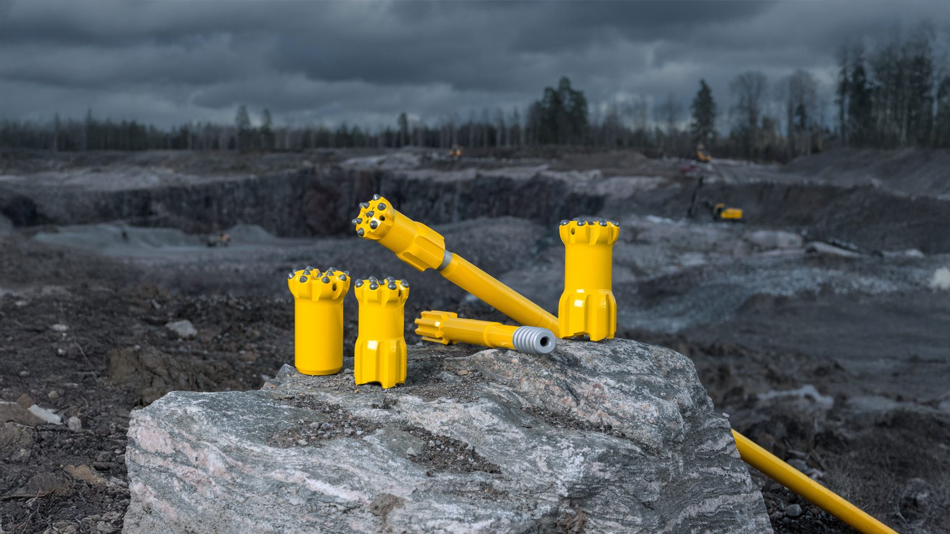 Yellow rock drill bits and rods for mining or construction, displayed on a rock in a quarry.