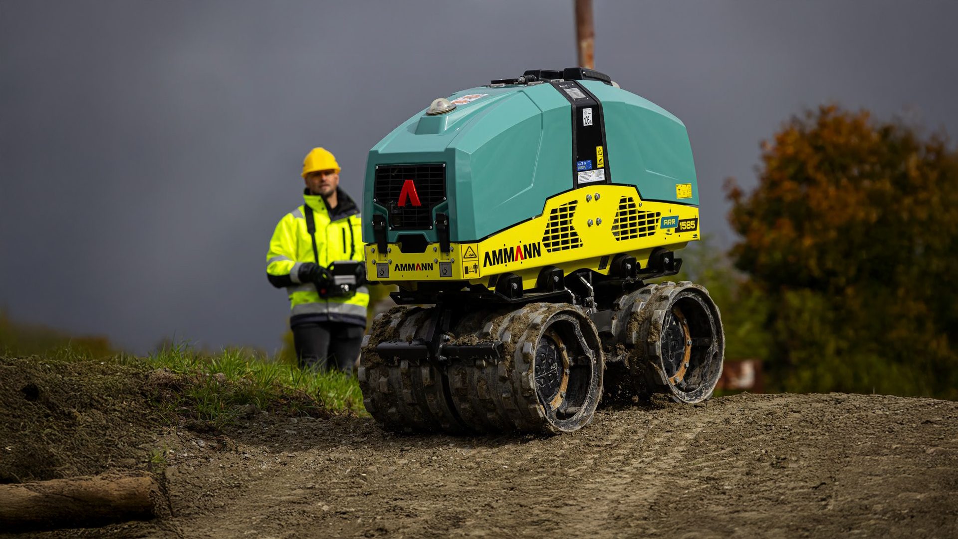 Worker operating an AMMANN ARR 1585 remote roller on dirt.