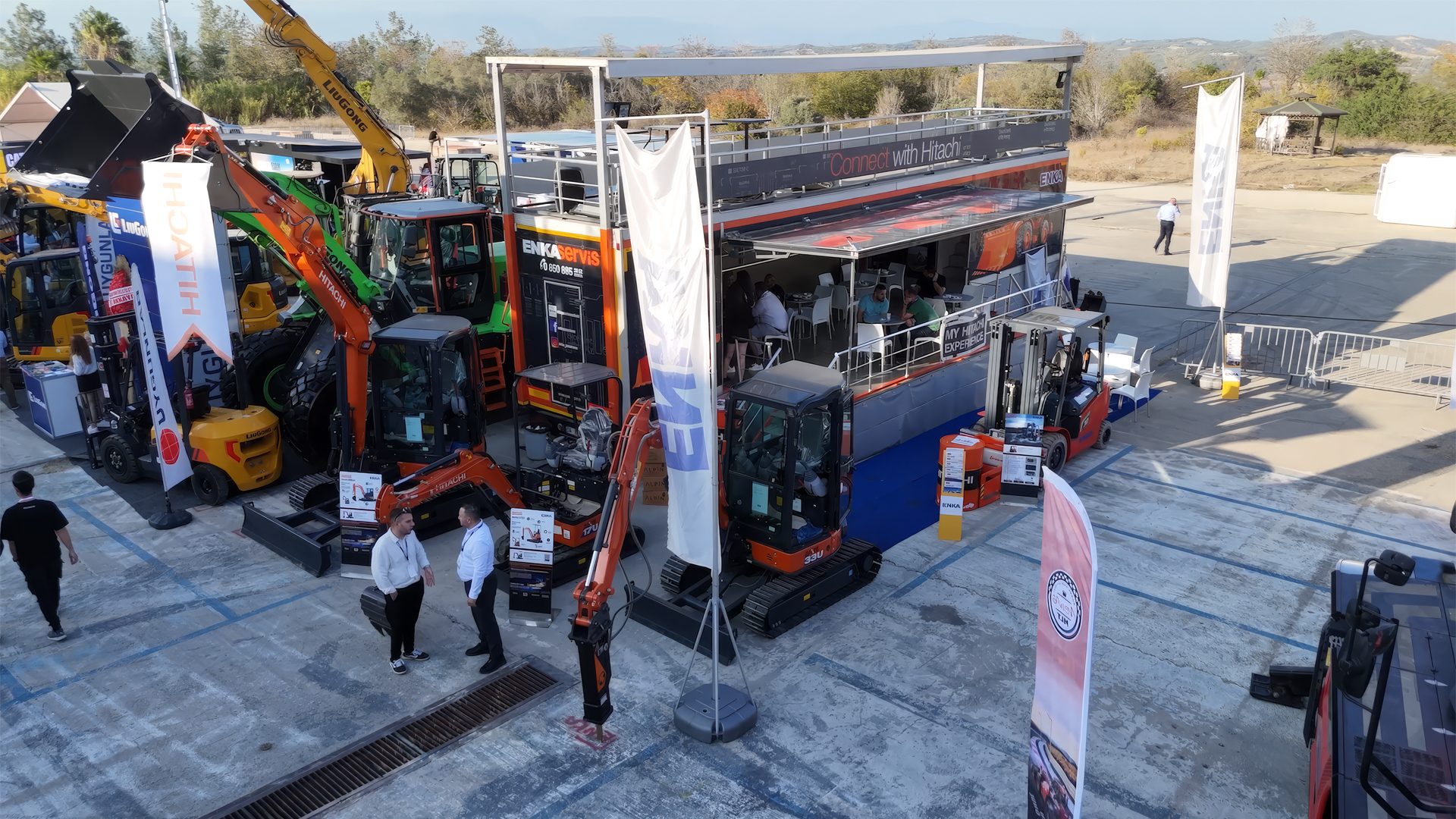 Outdoor display of Hitachi excavators and heavy machinery at an exhibition with a large vendor booth.