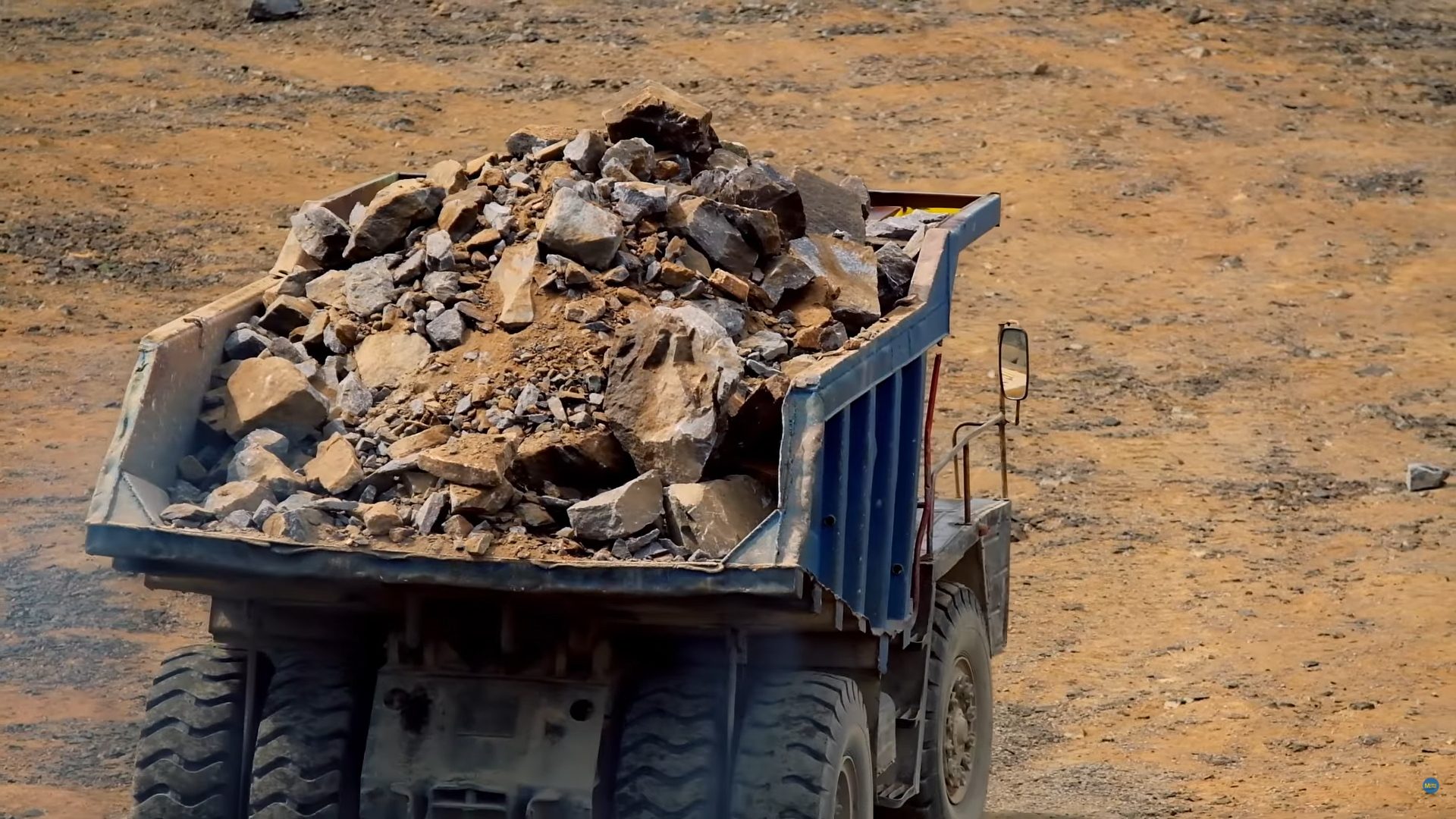 A large, heavy-duty dump truck loaded with a pile of rocks and dirt on a construction site.
