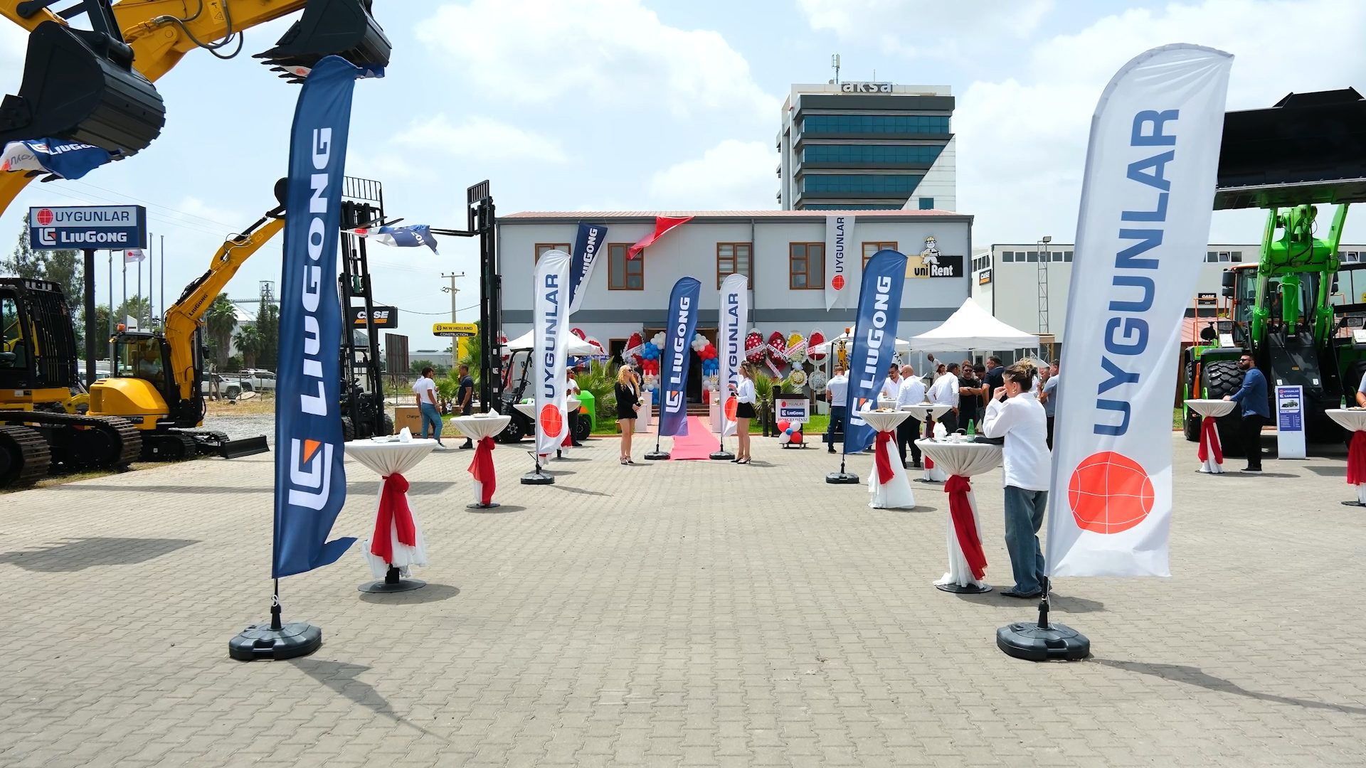 Outdoor construction equipment show with numerous LiuGong and Uygunlar flags and people.