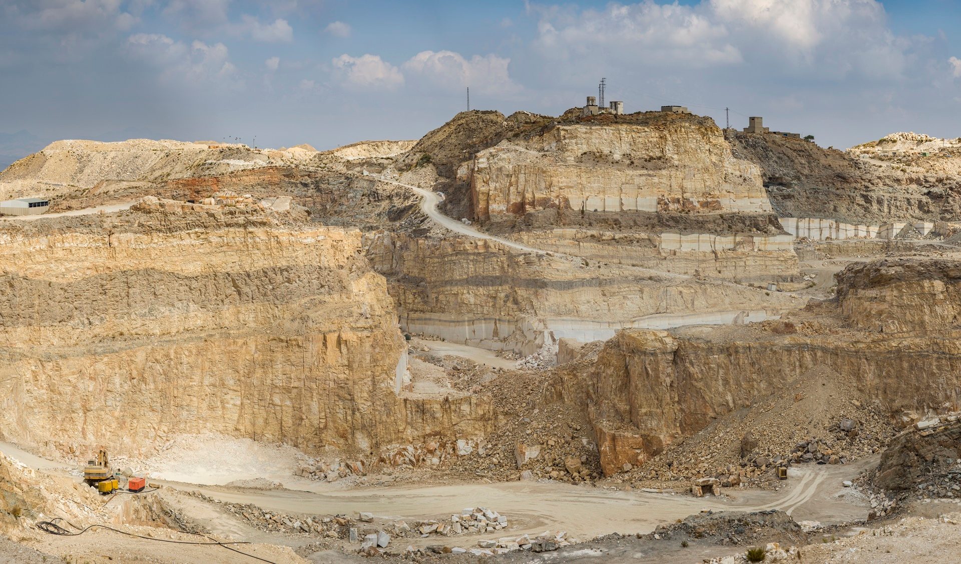 A vast terraced rock quarry in a desert mountain range, with dirt roads and mining equipment.