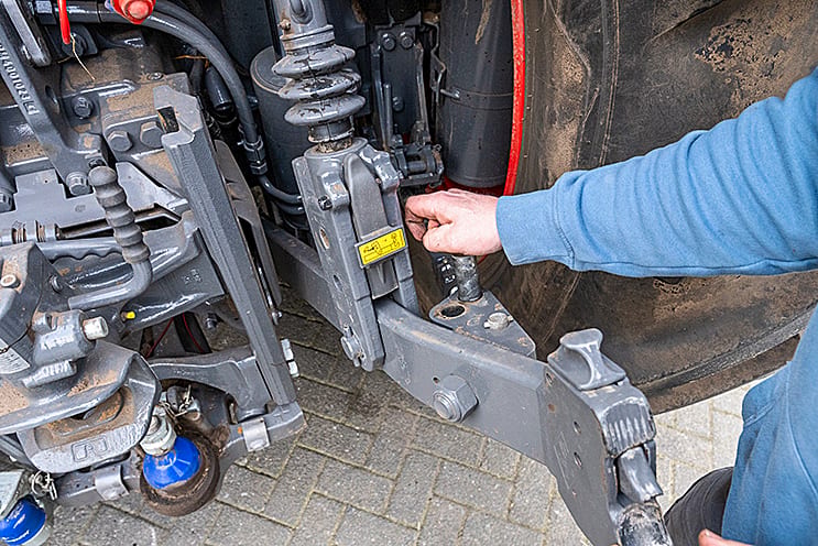 Hand adjusting a heavy machinery component on a tractor's rear linkage.