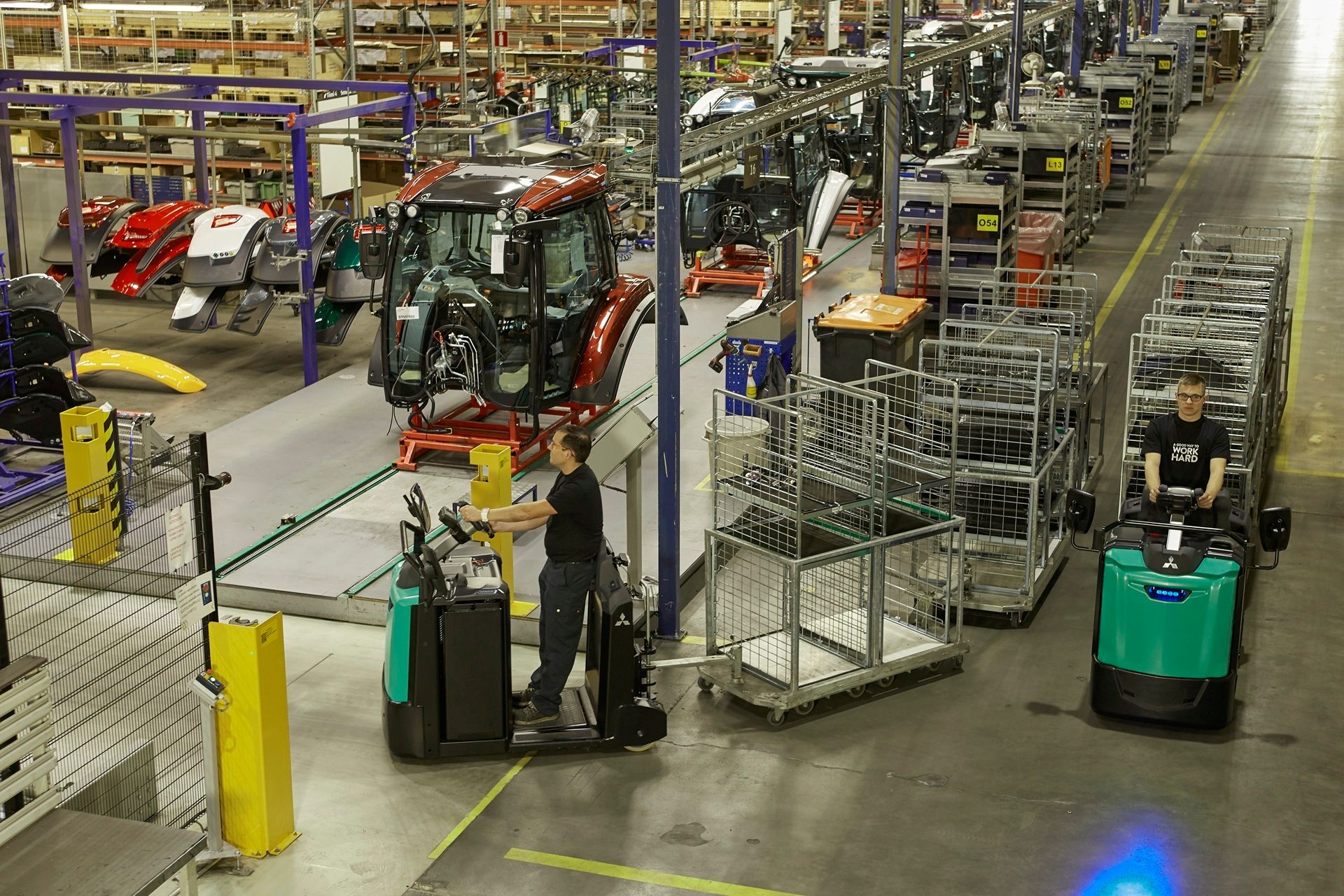 Workers assemble tractors on a production line in a large factory with materials and equipment.