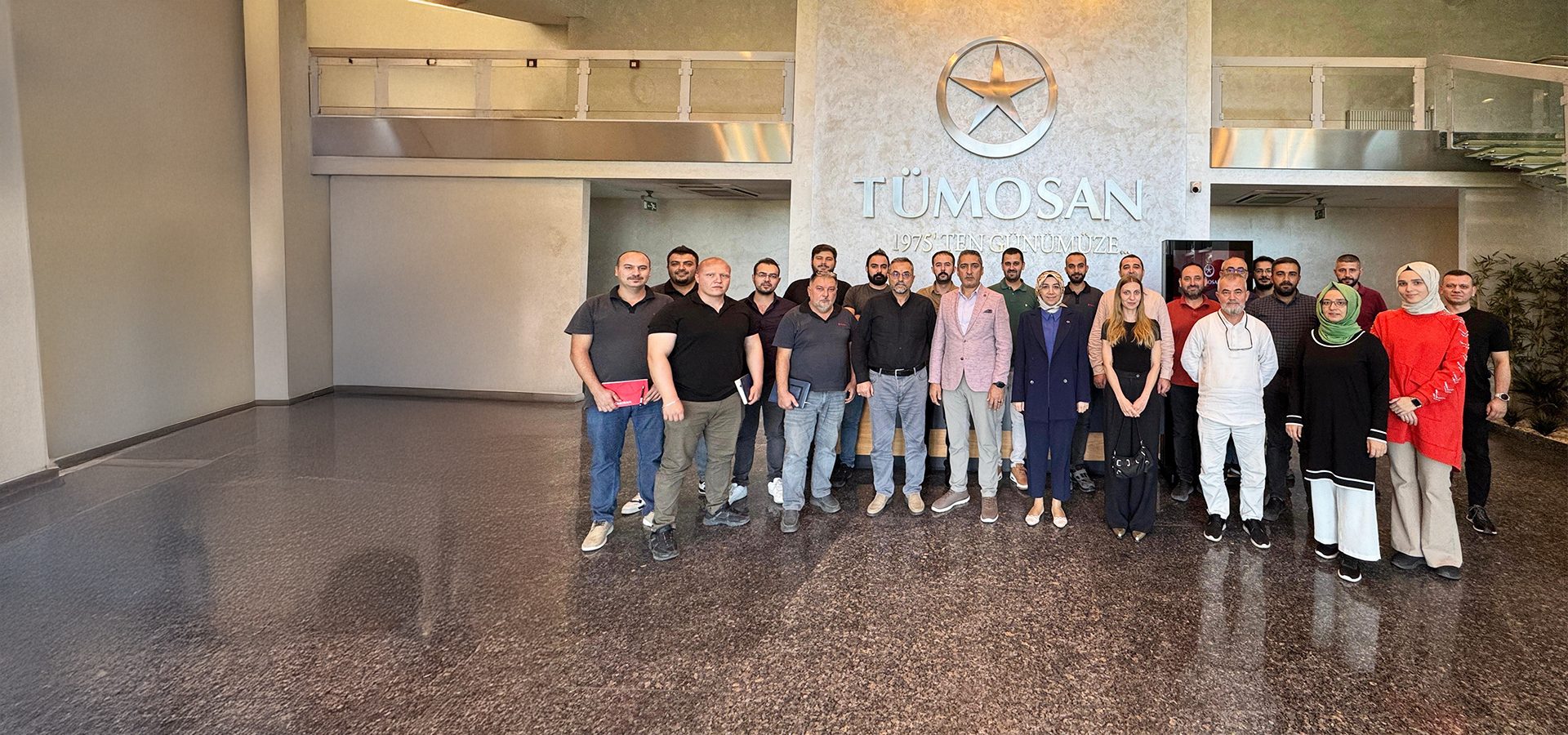 A group of diverse people stand in a modern lobby with the "TÜMOSAN" logo behind them.