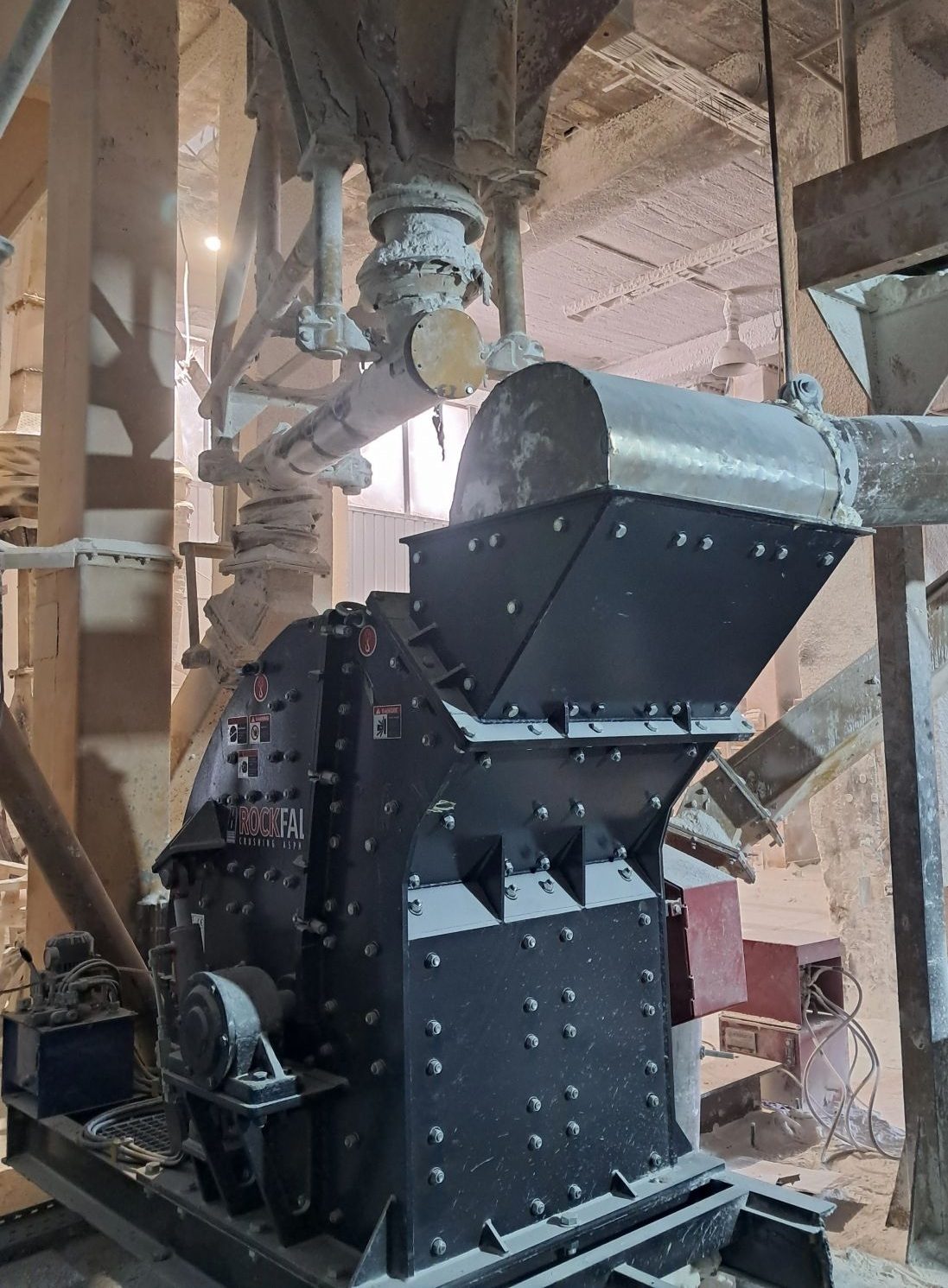 Industrial hammer mill, Rockfal brand, operating in a dusty factory setting.