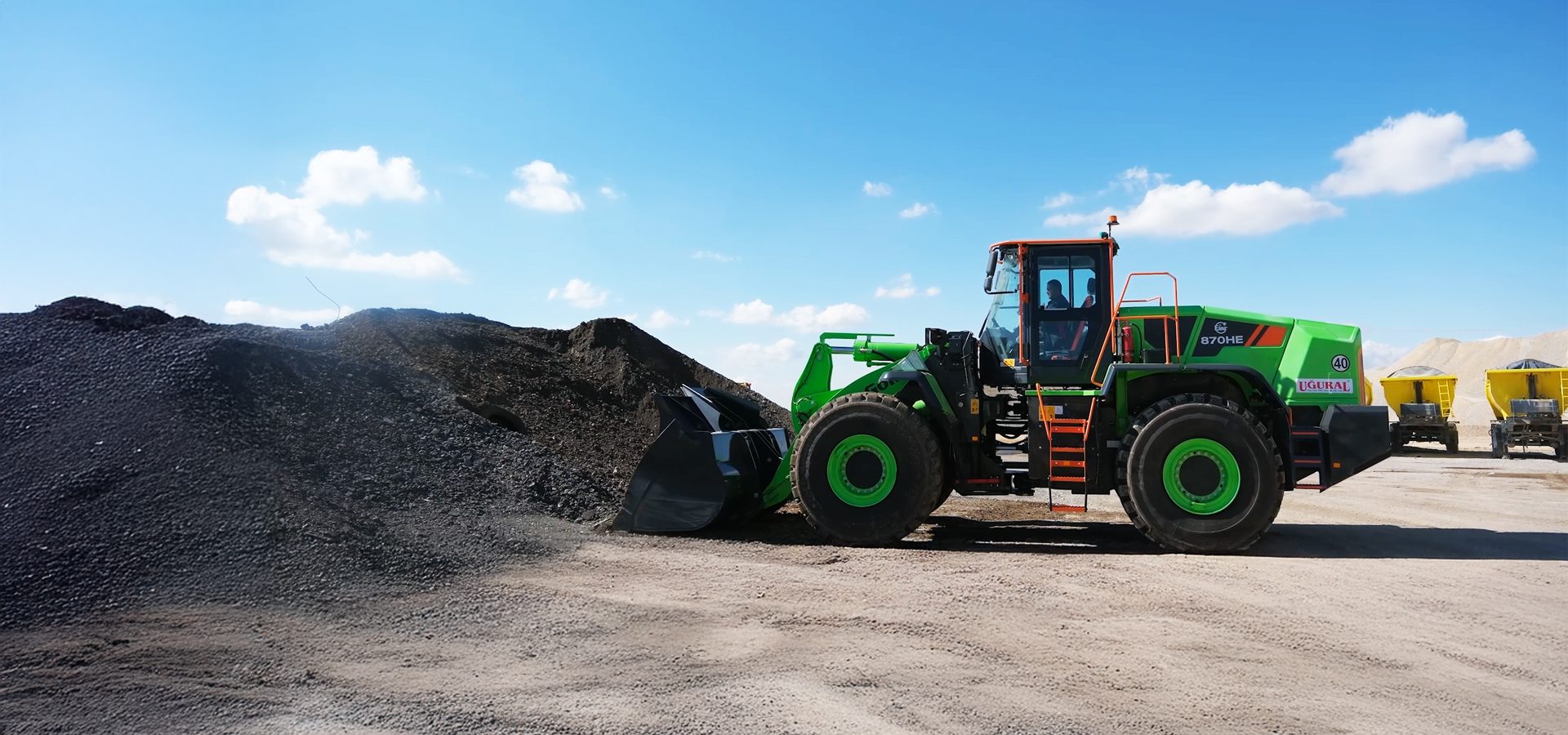 Large green front-end loader at a gravel site under a blue sky.