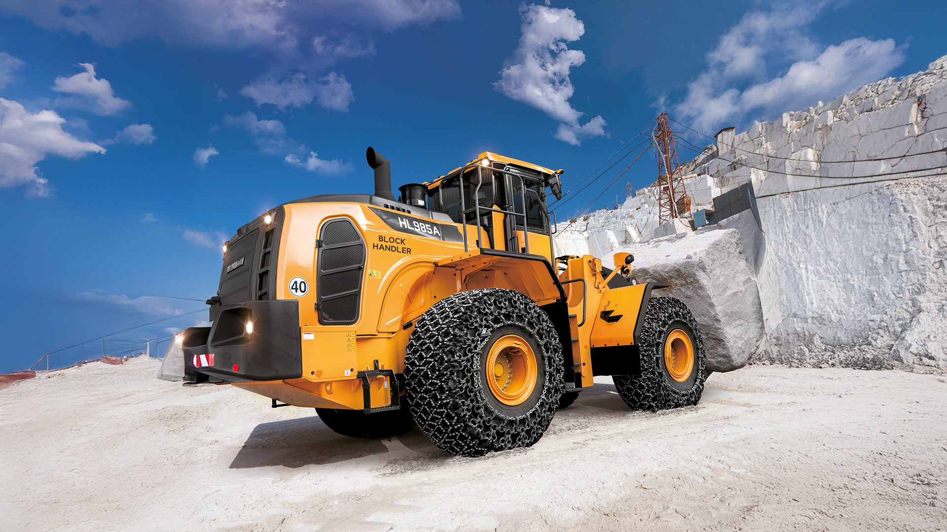 Yellow Hyundai HL985A Block Handler wheel loader with tire chains in a marble quarry.