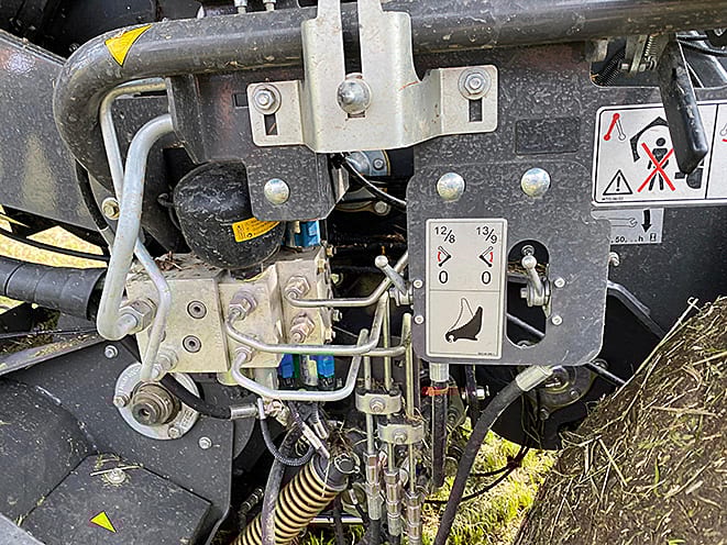 Hydraulic valves, hoses, and a control panel on agricultural equipment, with warning labels.