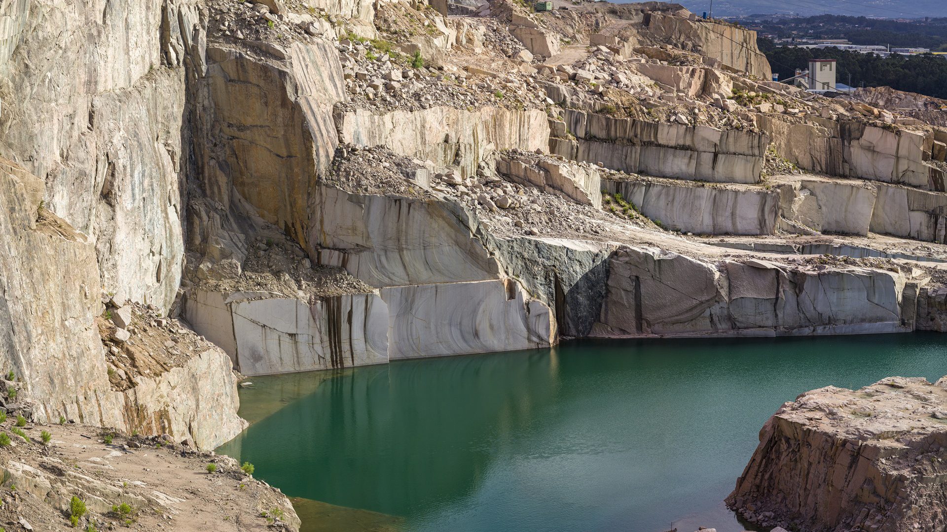 Massive terraced rock walls of an open-pit quarry with a deep, still turquoise-green lake at its base.