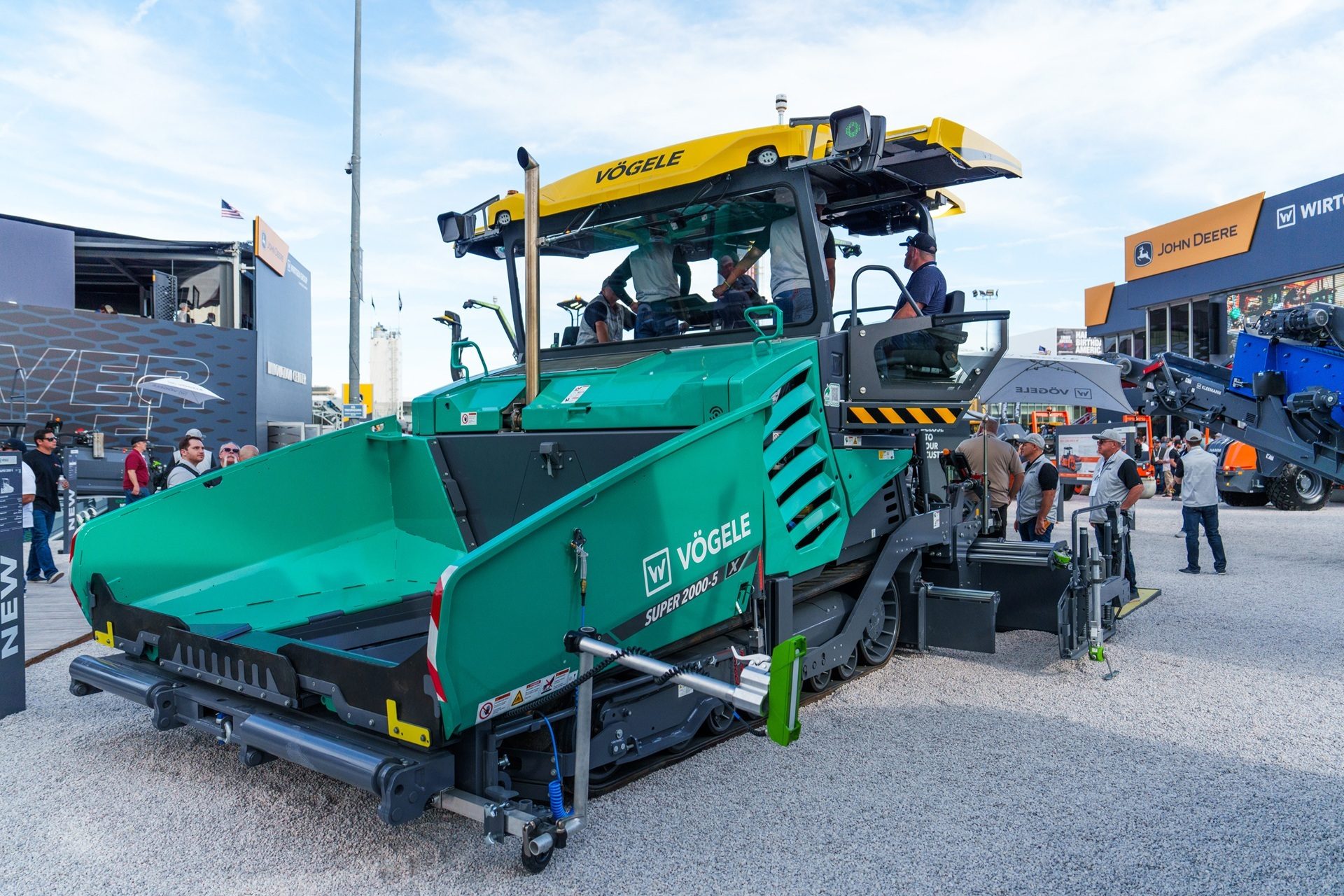 A large green and yellow Vögele SUPER 2000-3i asphalt paver at an outdoor exhibition with people.
