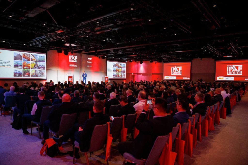 An audience watches a speaker on stage with multiple large screens displaying "2023 IPAF Summit" and presentations.