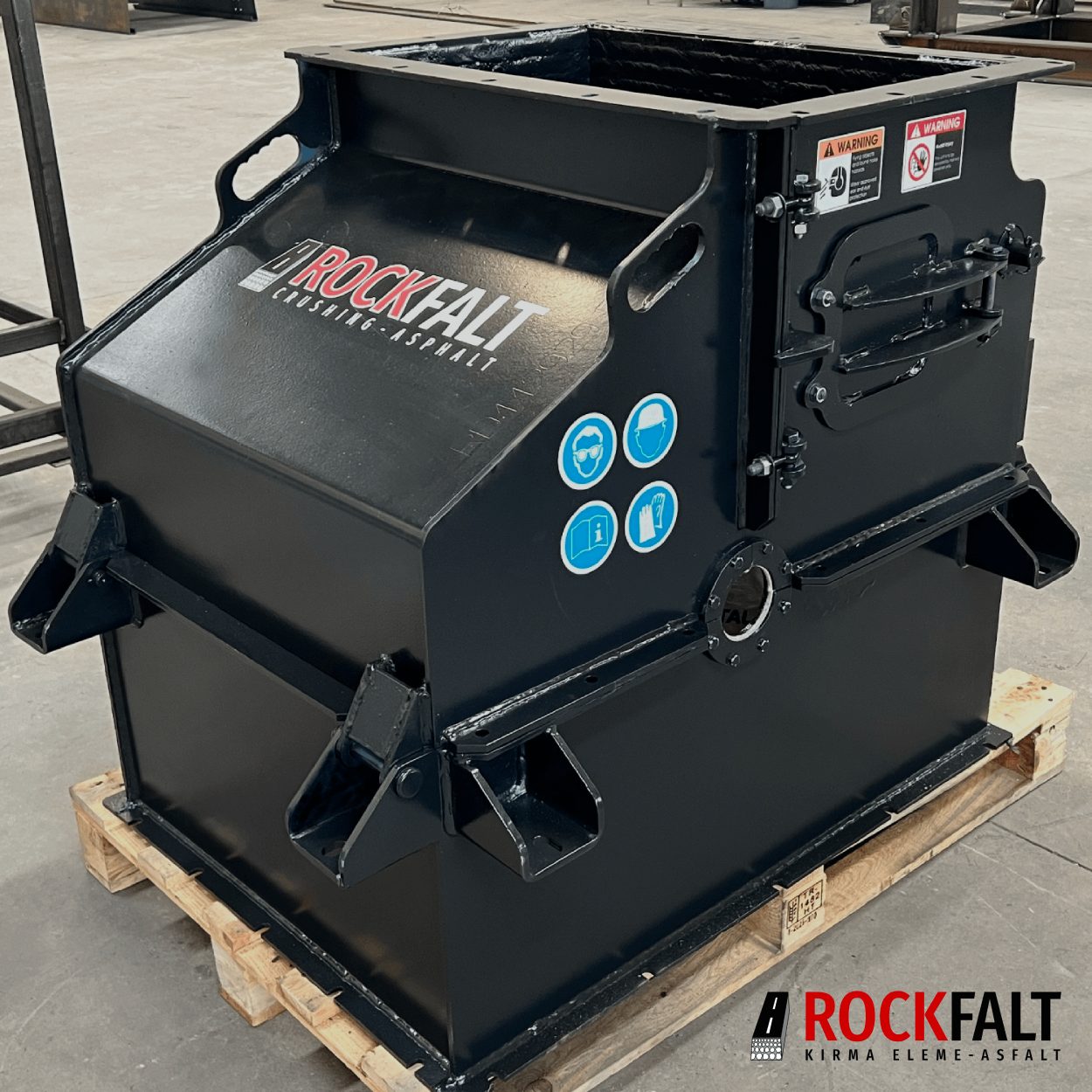 Black "ROCKFALT" industrial crusher on a pallet with safety warnings and PPE symbols.