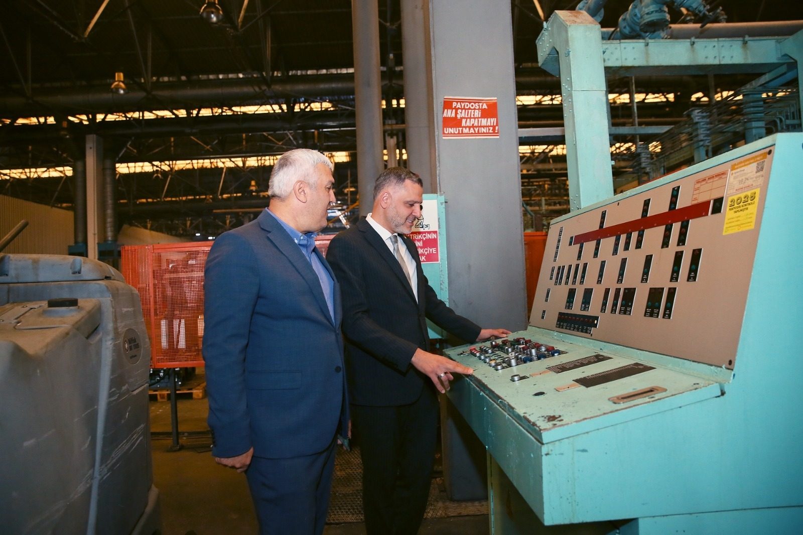 Two men in suits examining an industrial control panel in a factory.
