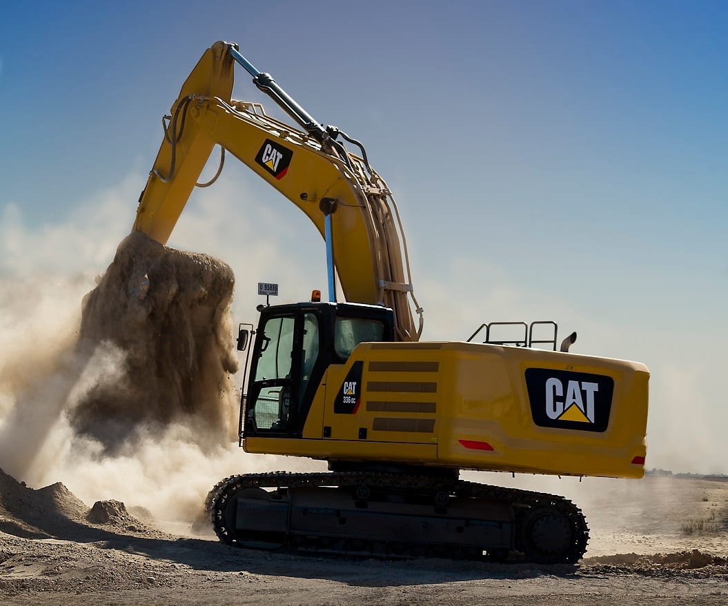Yellow CAT 336 GC excavator digging dirt, creating dust under a blue sky.