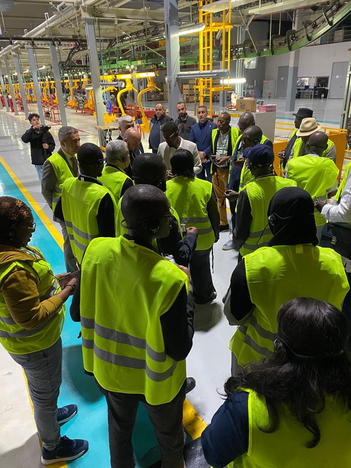 A diverse group in yellow safety vests and headphones gathered in a factory setting.
