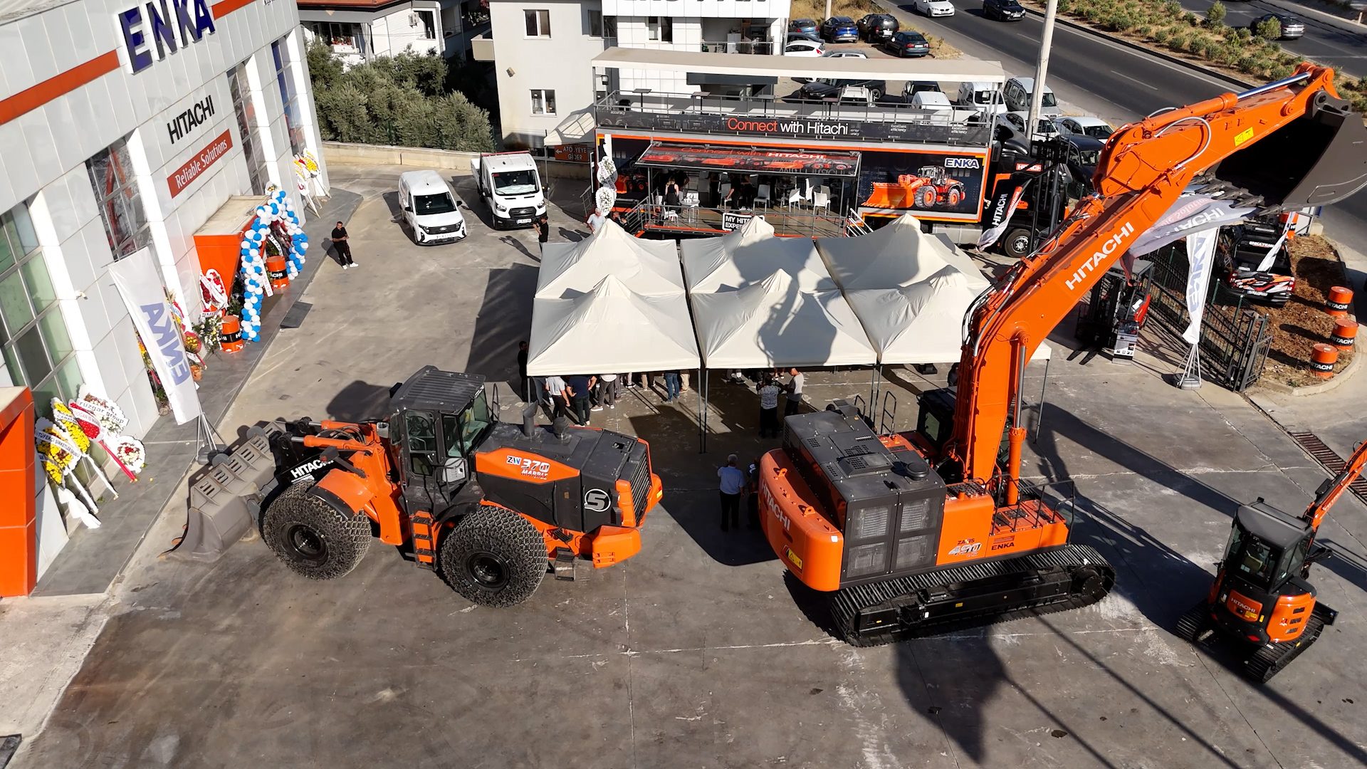 Hitachi-ENKA heavy equipment showcase event with excavators, loaders, tents, and attendees.