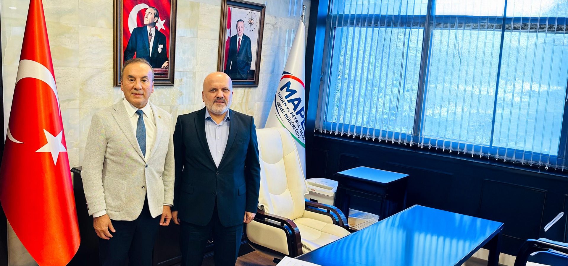 Two men in suits stand in an office with Turkish and MAPEG flags, and portraits of Atatürk and Erdoğan.
