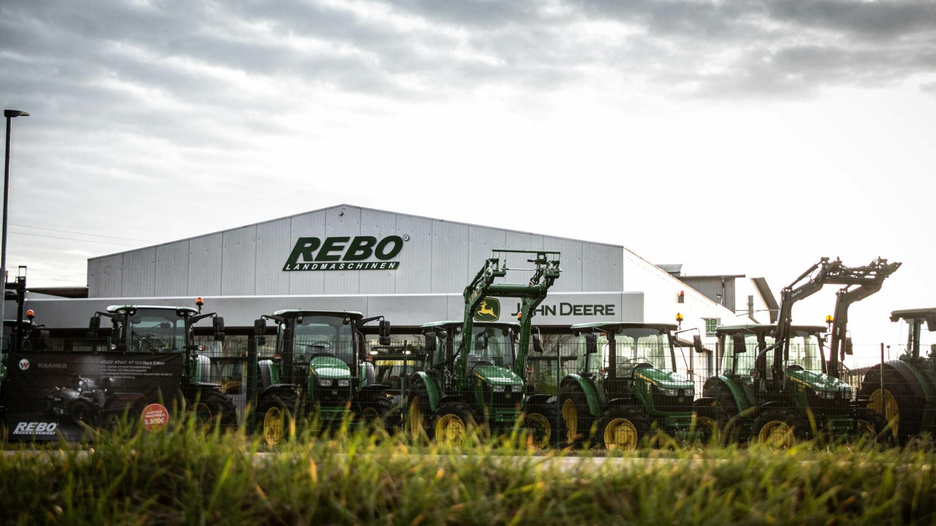 John Deere tractors parked outside a REBO Landmaschinen dealership building.
