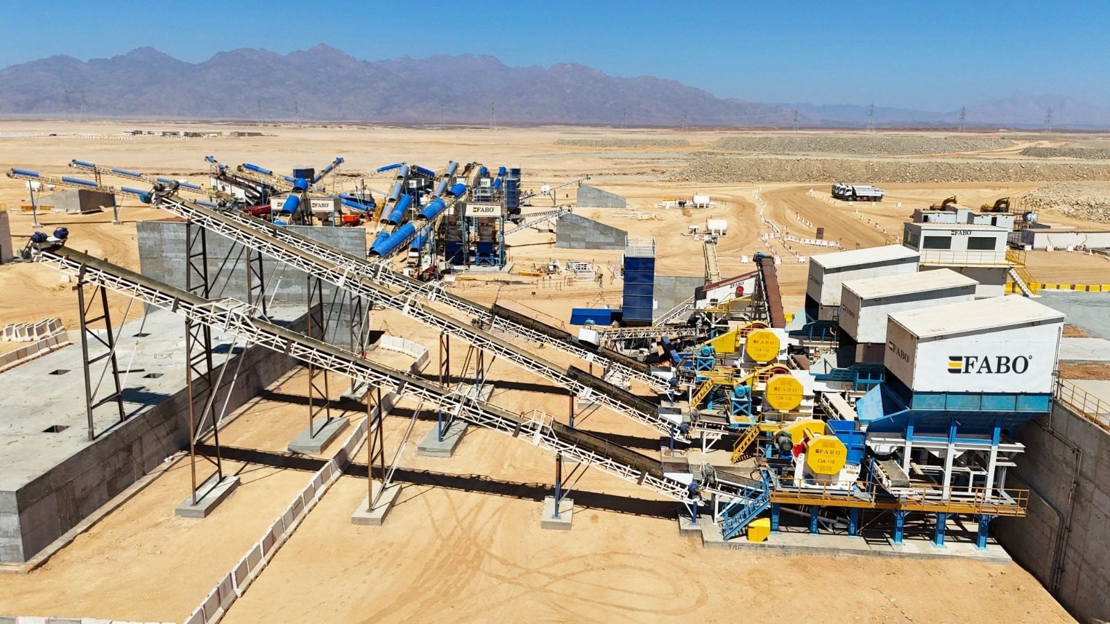 Aerial view of a FABO aggregate crushing plant in a desert landscape with mountains.