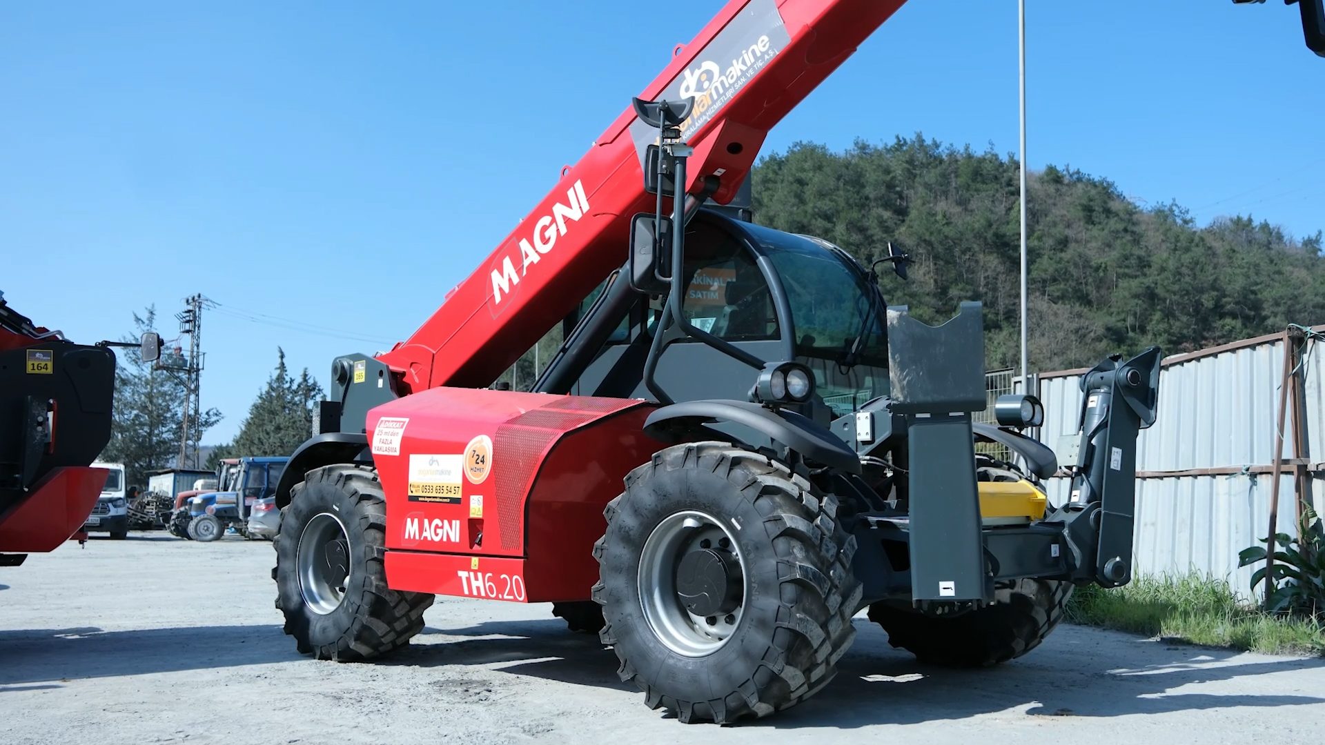 A powerful red Magni TH6.20 telehandler with a long boom and large tires, parked outdoors on a sunny day.