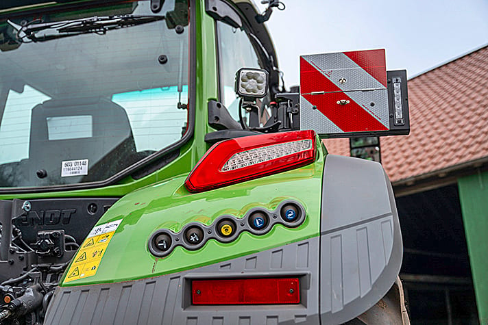 Close-up of a green tractor's rear with tail light, warning sign, work light, and control panel.