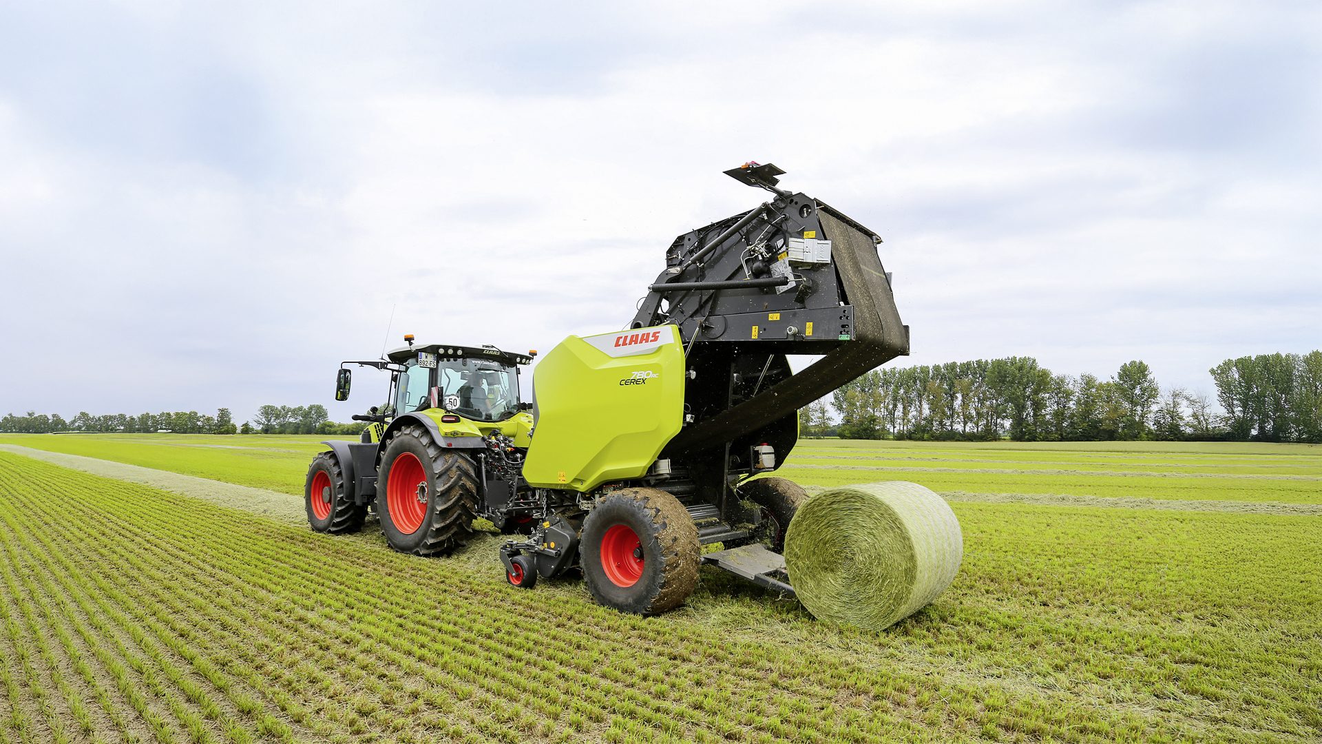 Claas tractor and baler dropping a round hay bale in a field.