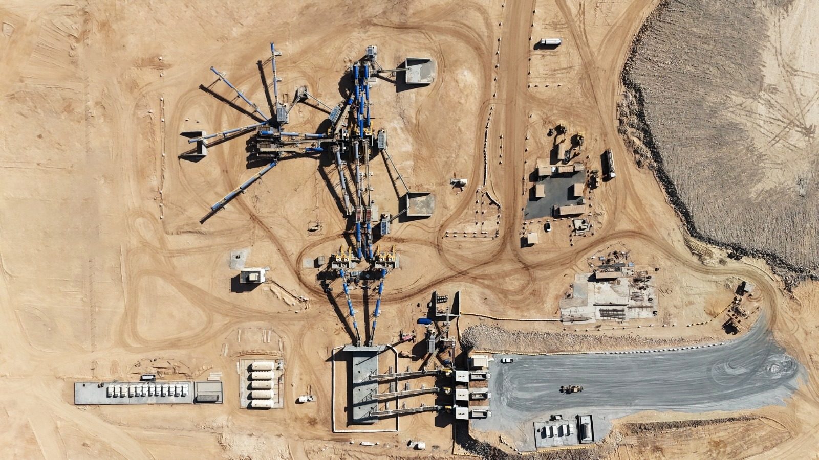 Aerial view of a desert mining facility with extensive machinery, structures, and excavated areas.