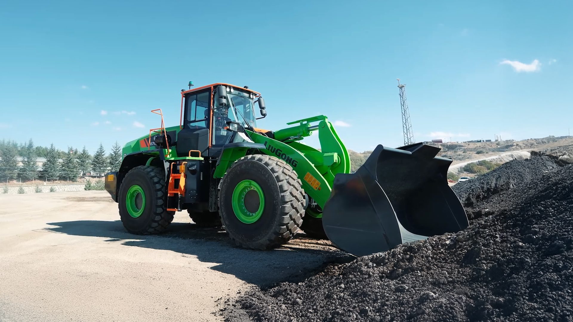 A green and orange wheel loader digging into a dark pile outdoors.