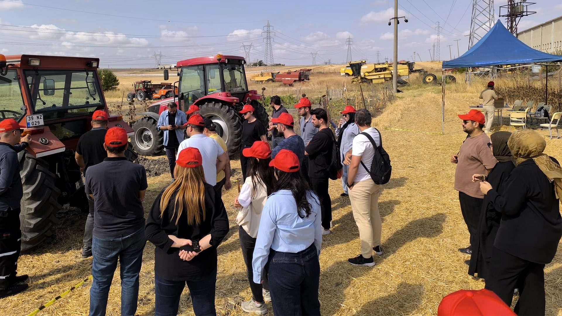 People in red hats gathered around red tractors in a dry field under a clear sky.