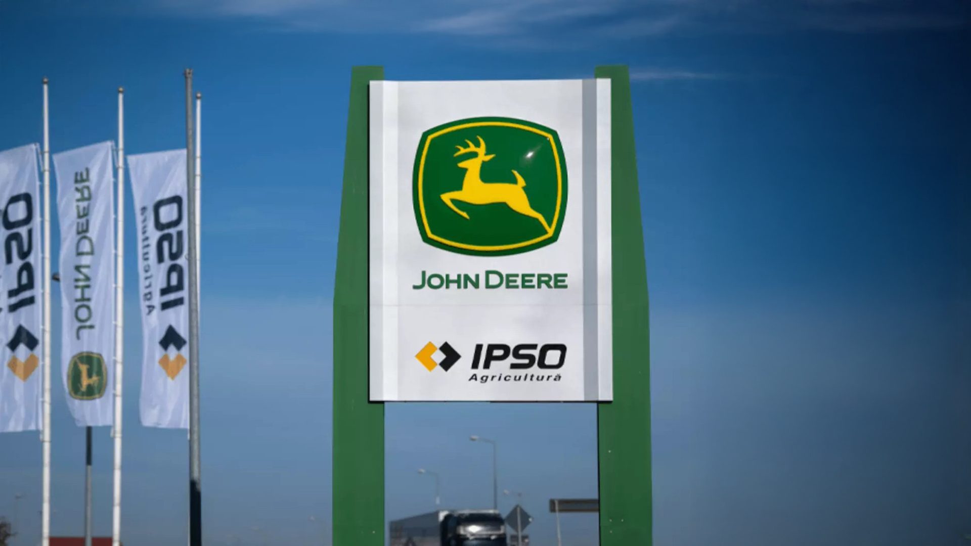 John Deere and IPSO Agricultura signs and flags against a blue sky.