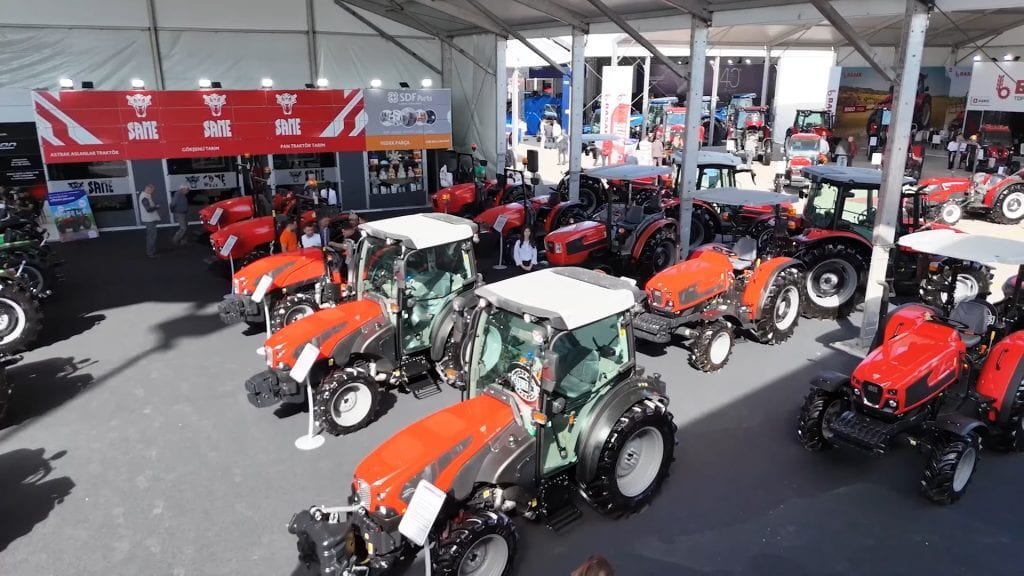 Indoor exhibition displaying rows of new orange and red tractors.