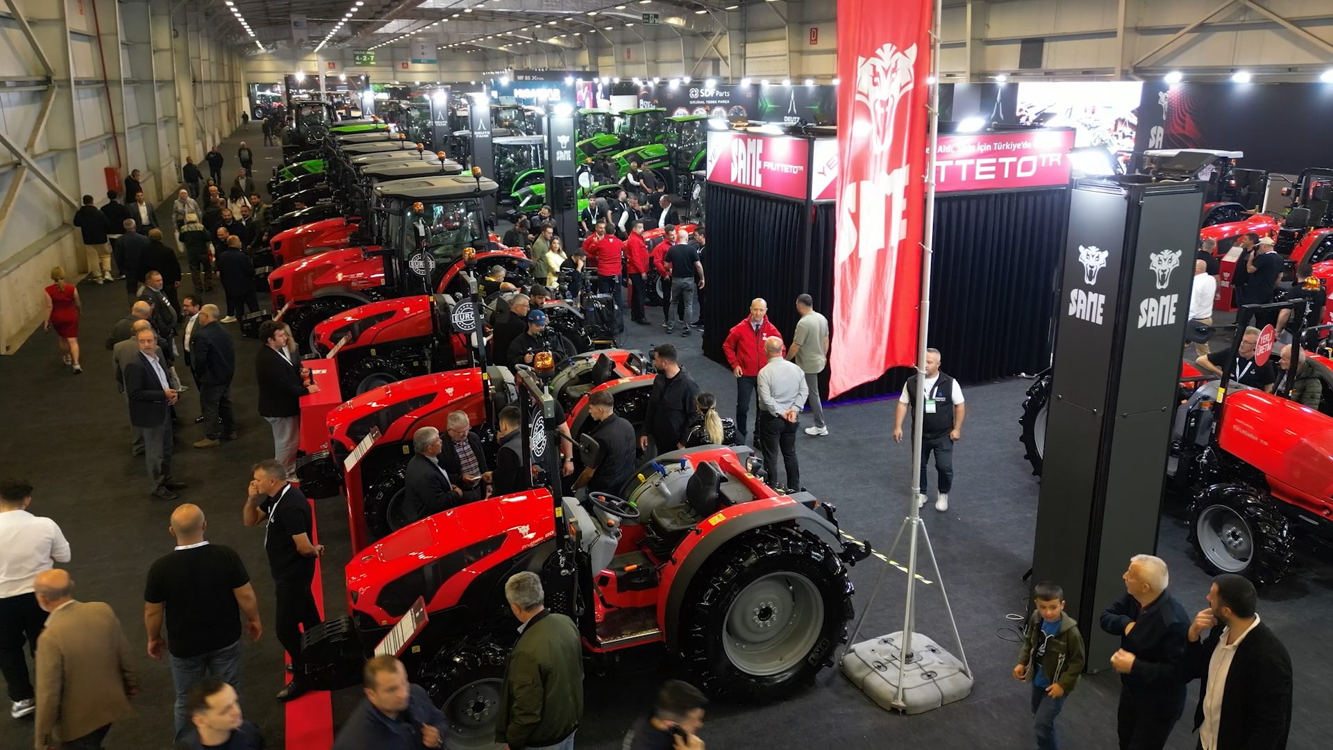 Indoor agricultural trade show with many red and green tractors on display and attendees.