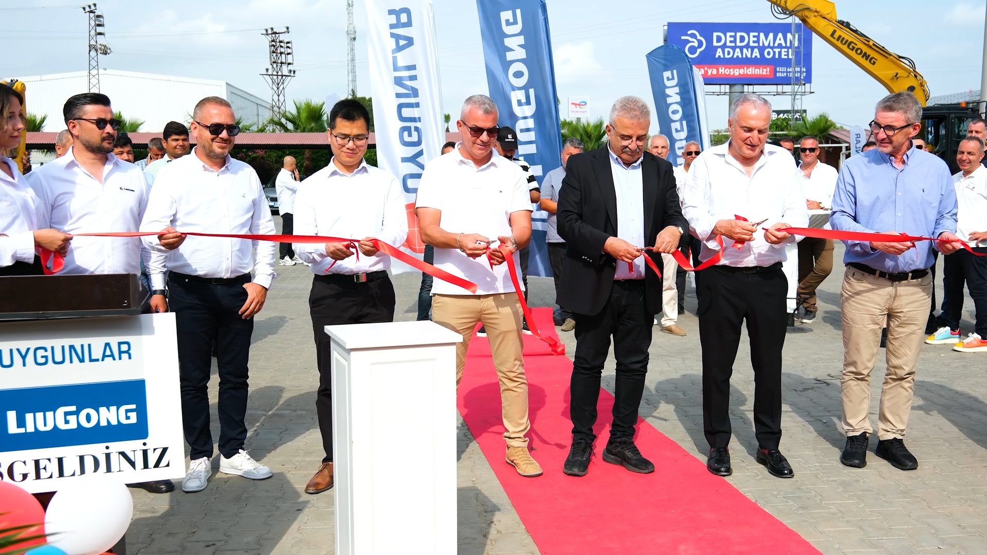 Outdoor ribbon-cutting ceremony with multiple people, LiuGong and Dedeman Hotel branding.